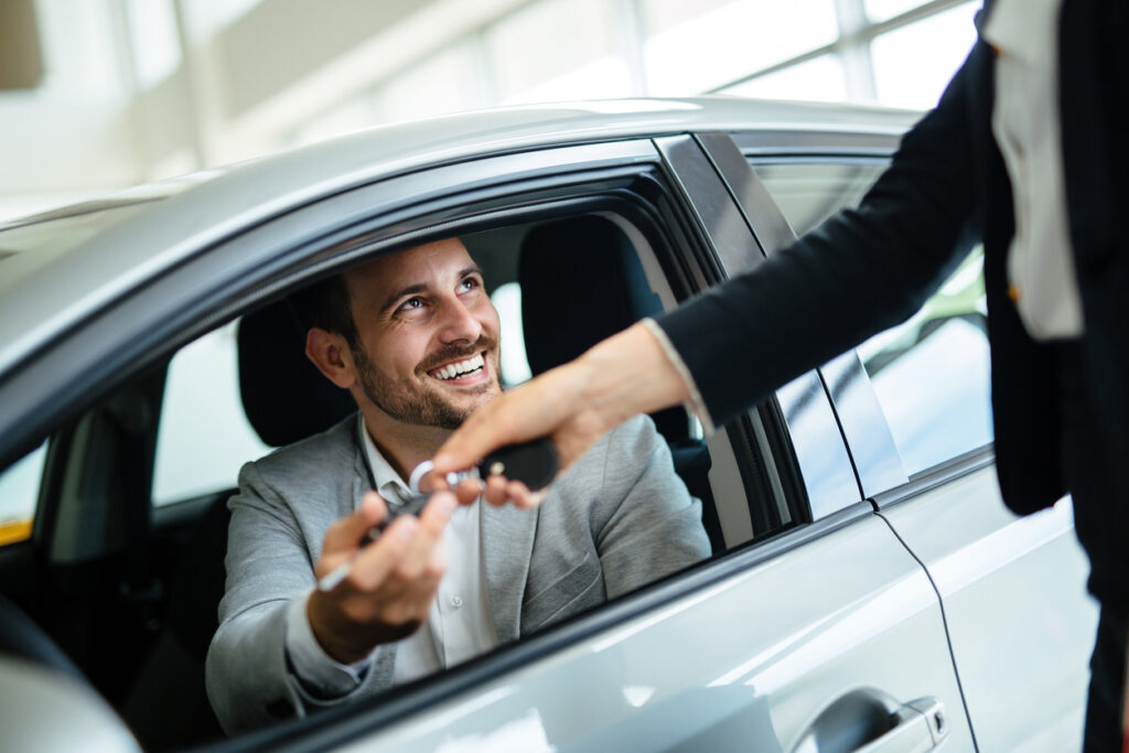 Man smiling in driver's seat being handed keys of his new hybrid import from Japan